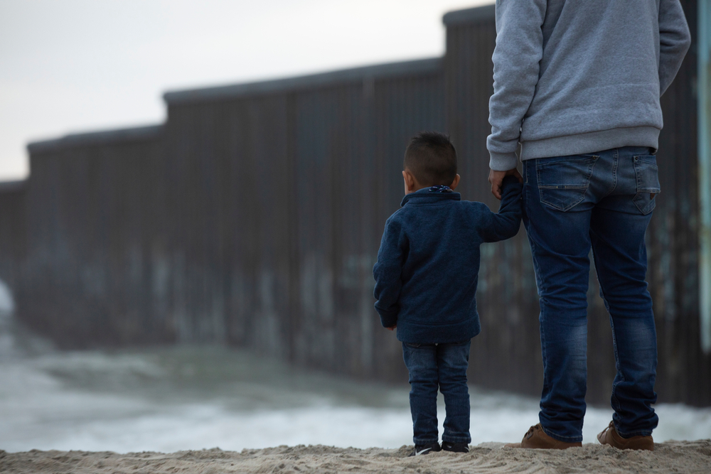 Child with parent by U.S.-Mexico border wall