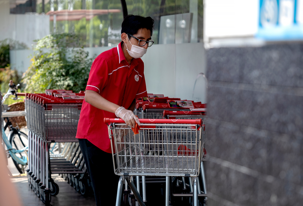 Supermarket worker disinfecting shopping carts and wearing a mask amid coronavirus outbreak in South America. Cleaning shopping carts outside a Wong store in COVID-19 times.