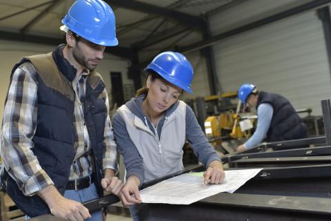 Woman and man in hardhats work together on plans on construction site
